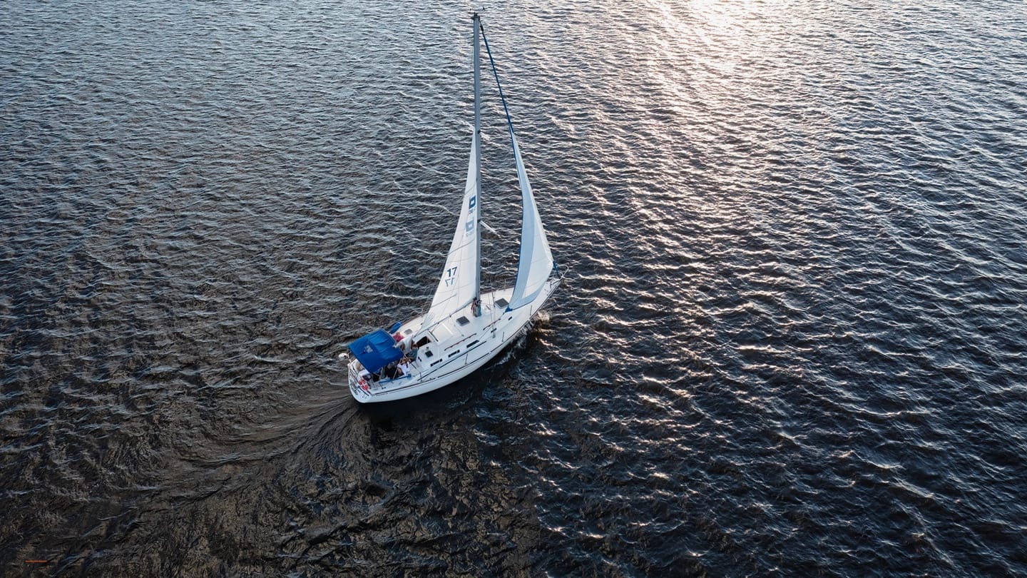 White sailing yacht crossing clear blue water from an overhead view