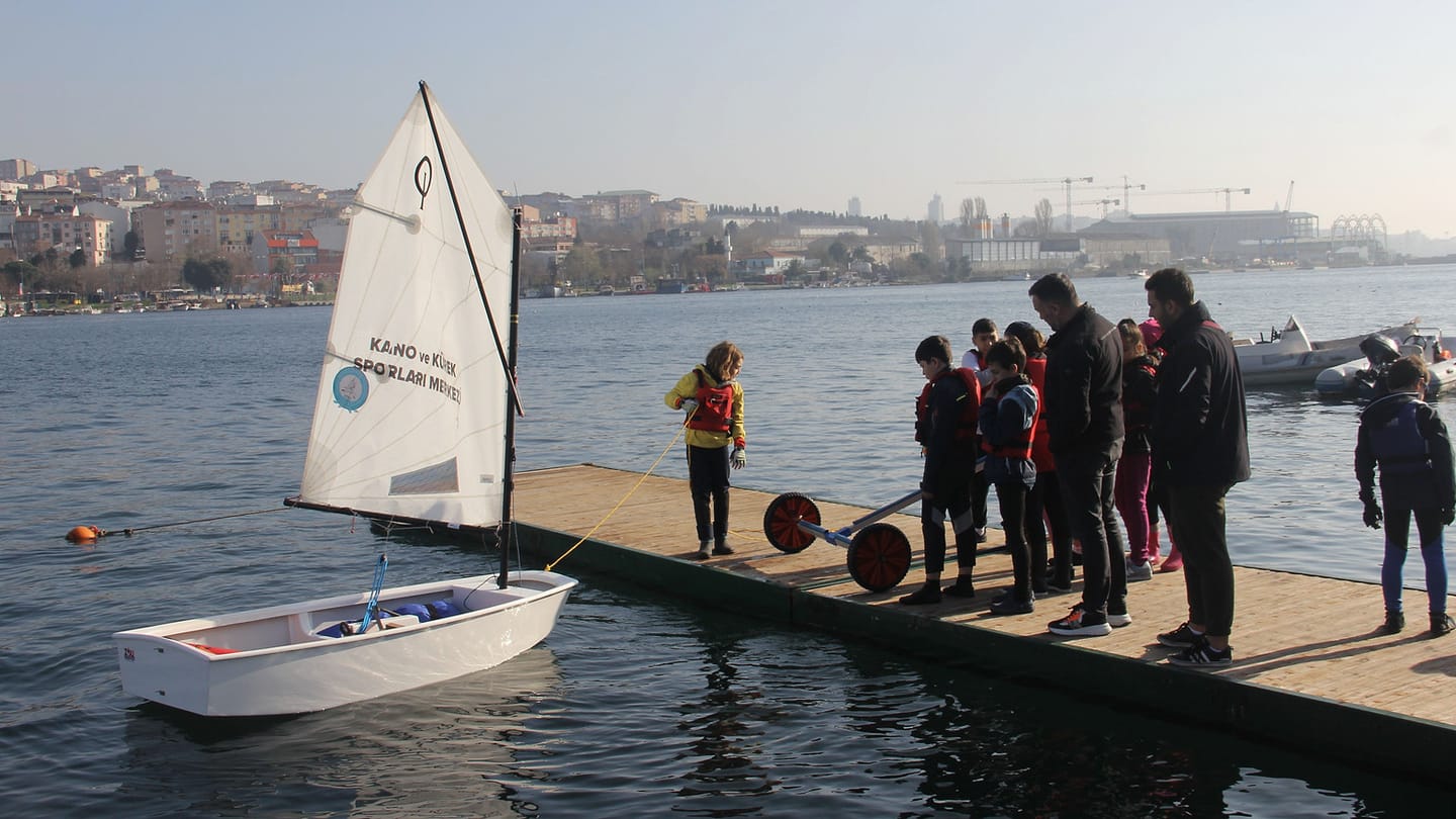 A life-jacketed group beside a small sailing dinghy