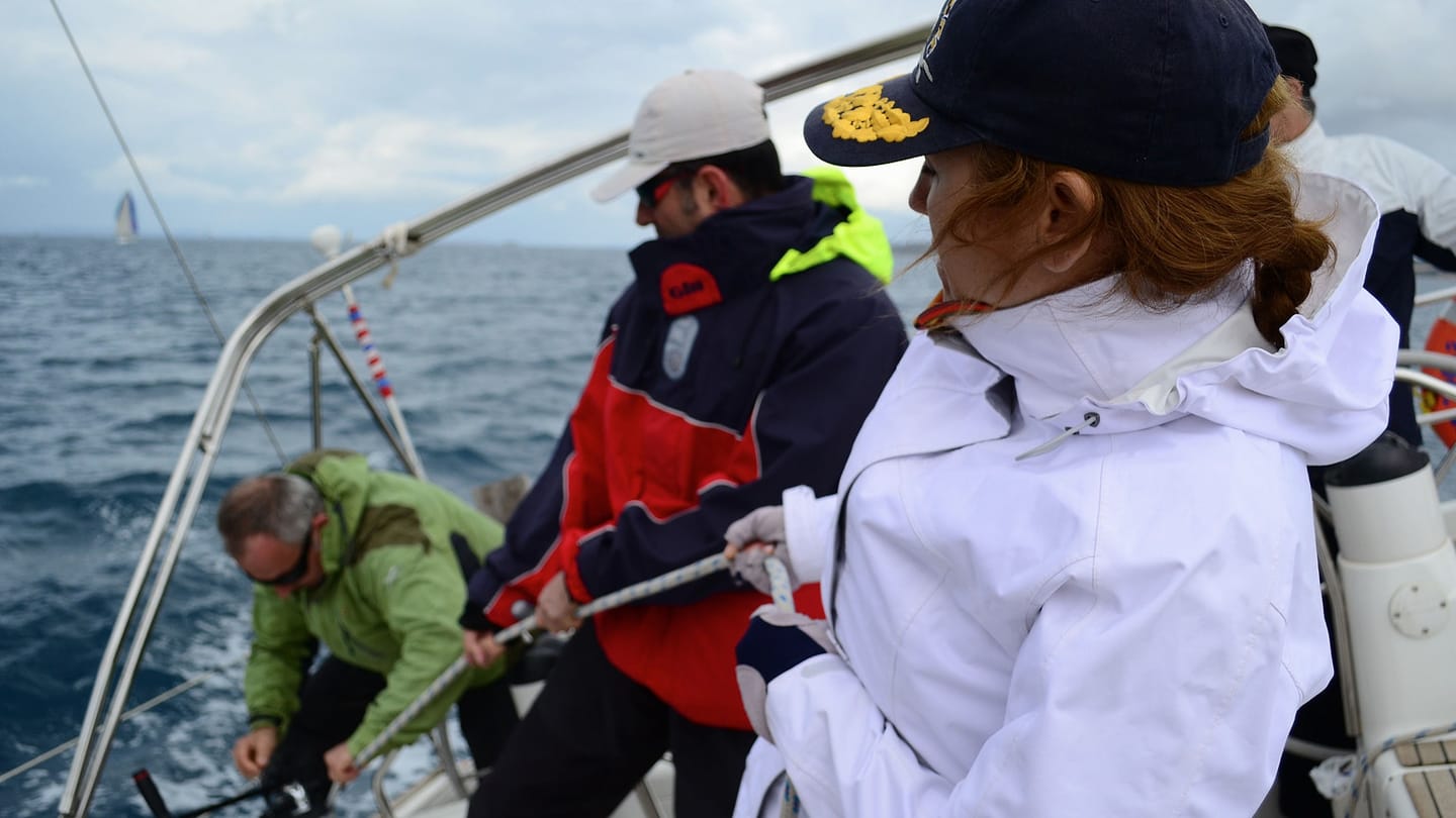 Three crew members on the deck of a heeled yacht