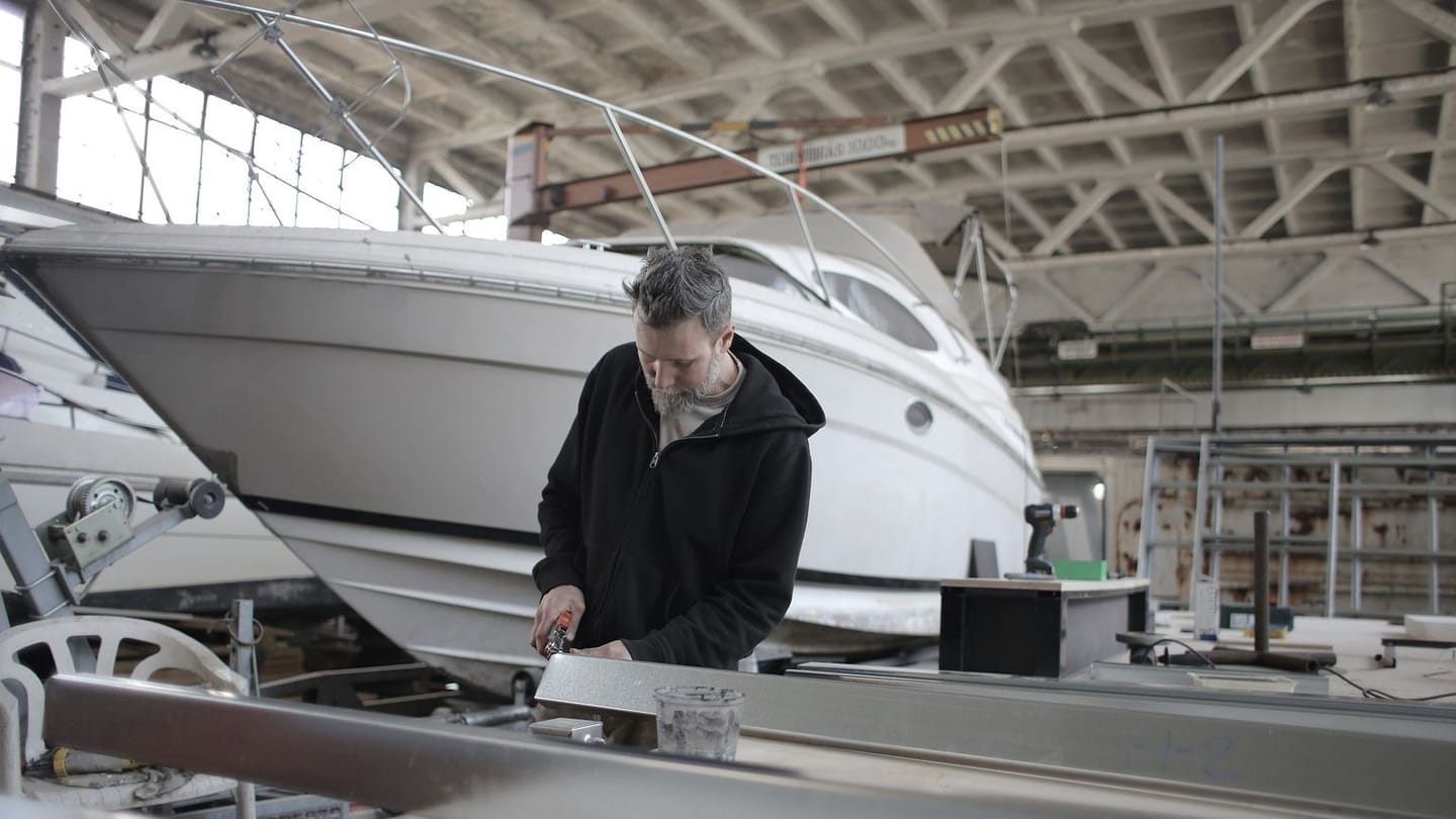 A technician beside a hauled yacht in an indoor workshop