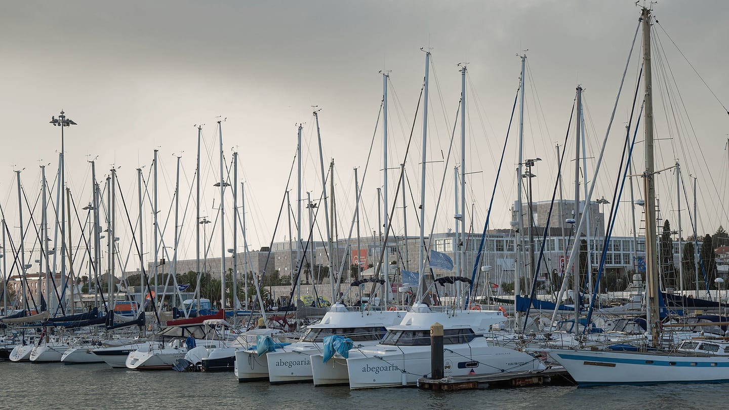 An instructor and crew prepare a sailboat beside a sheltered marina.