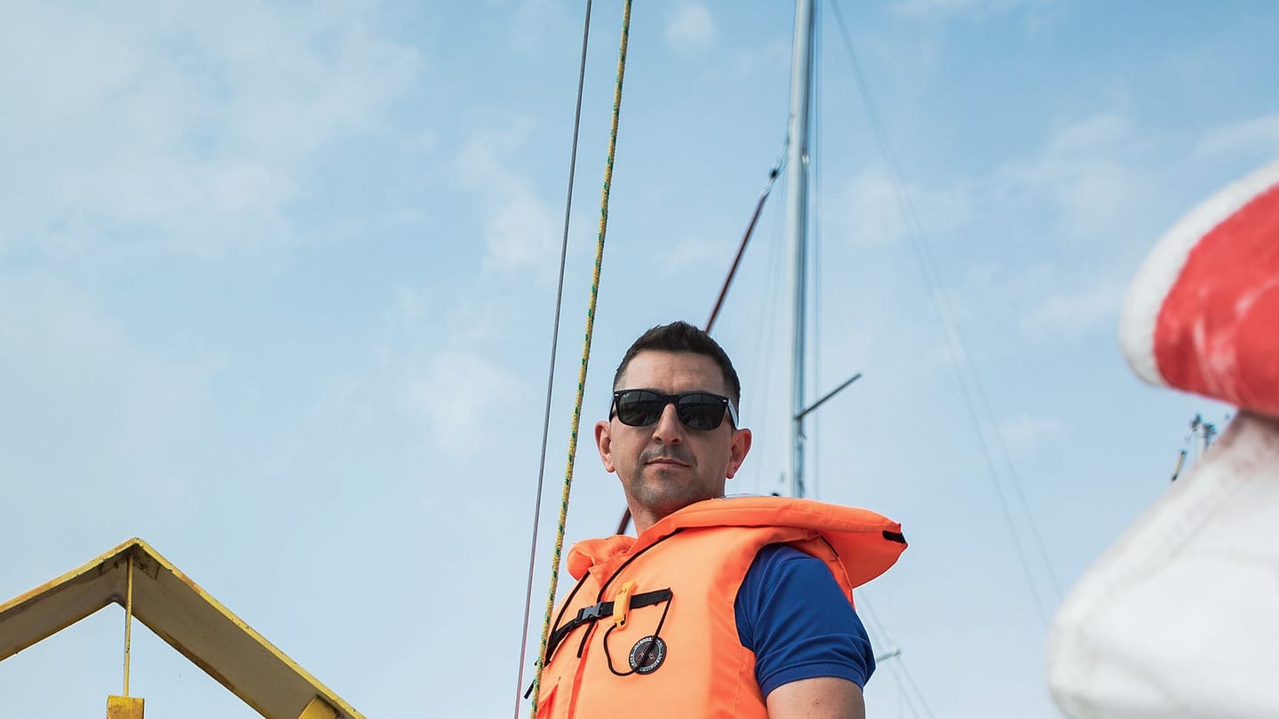 A sailor works on deck wearing close-fitting sailing clothing and safety gear.