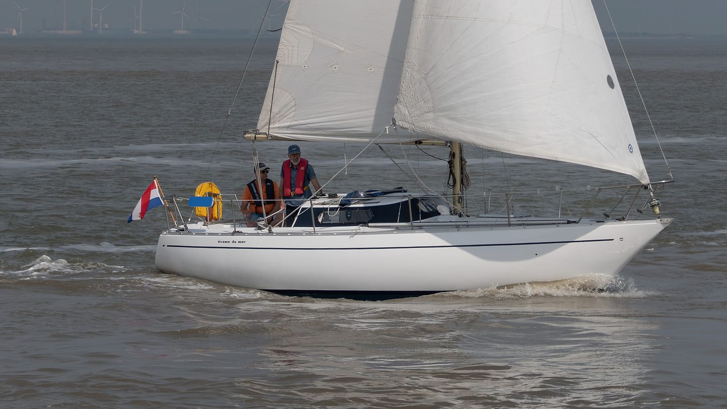 A sailing crew talks beside the mast before leaving sheltered water.