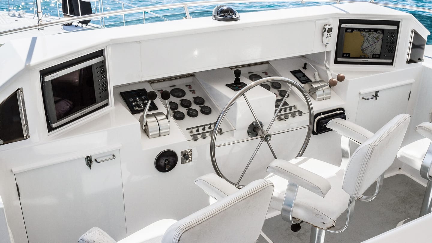 A boat helm shows a wheel and electronic navigation instruments.