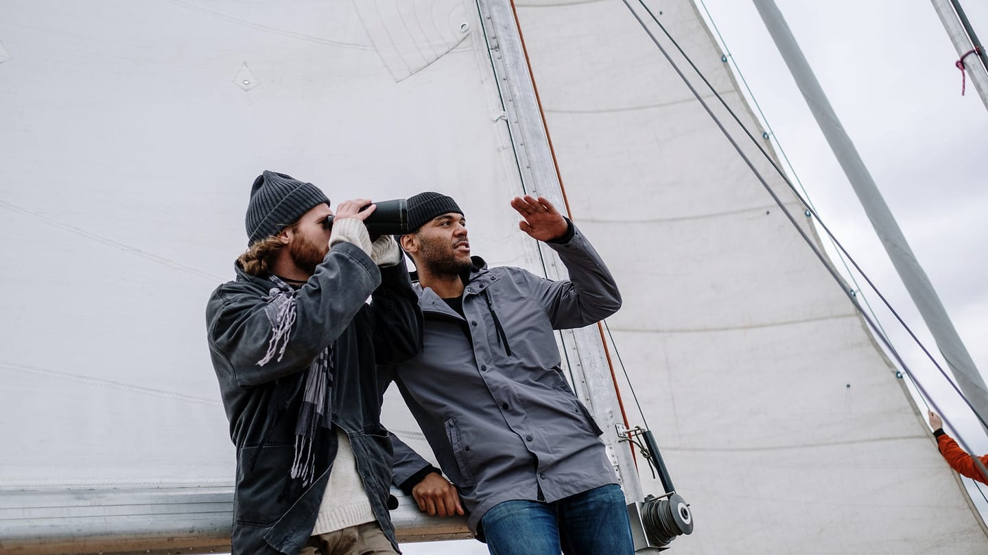 Two sailors scanning ahead beside the raised sail of a yacht