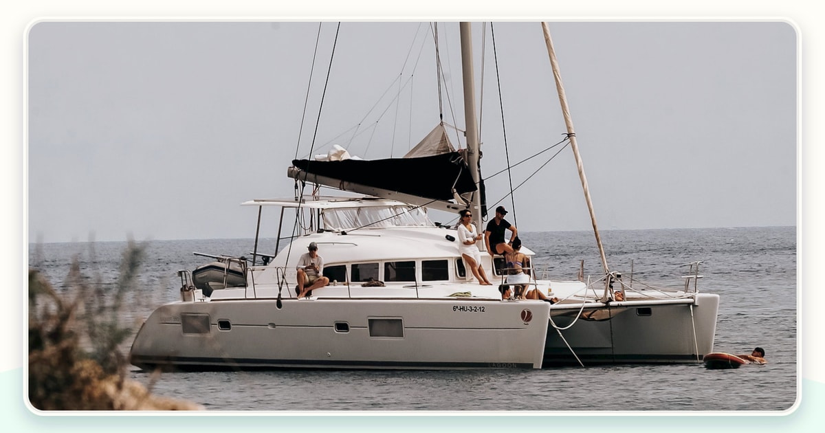 Guests sharing a relaxed meal in a yacht cockpit while crew work safely in a separate galley area