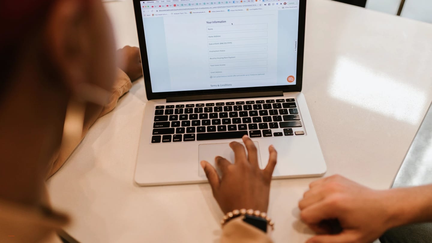 Hands using a laptop form beside a notebook and printed papers