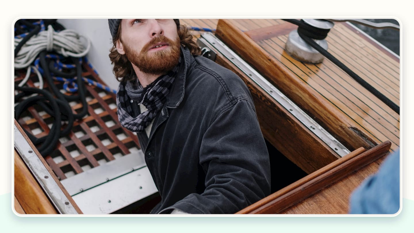 A sailor emerging through an open deck hatch on a sailboat