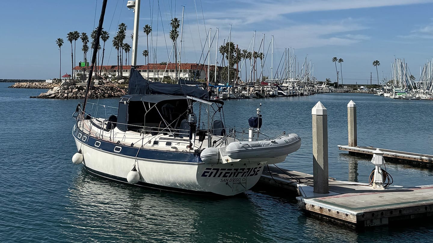 A moored sailboat rests against fenders with lines leading to the dock.