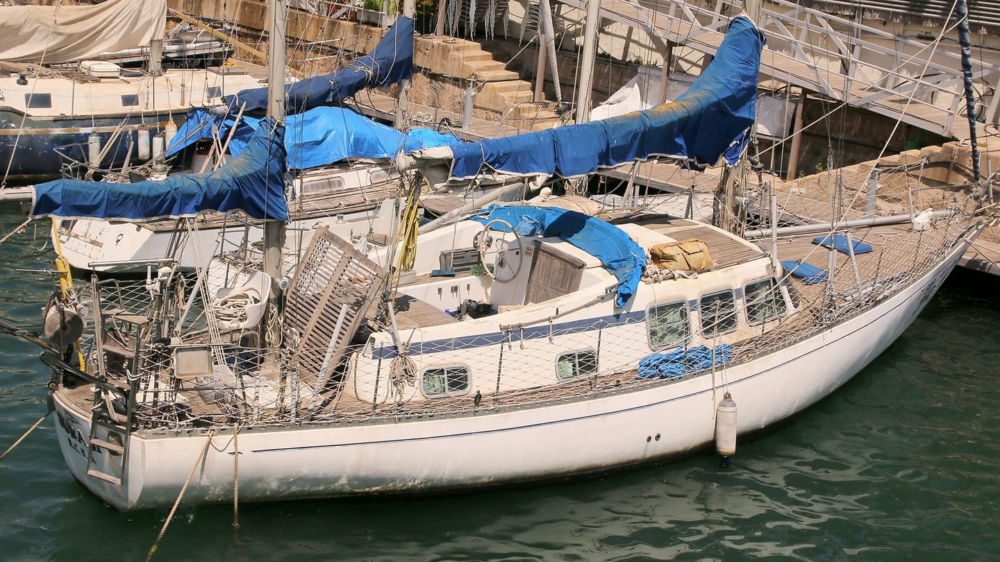 A sailboat moves through a marina entrance with open water available ahead.