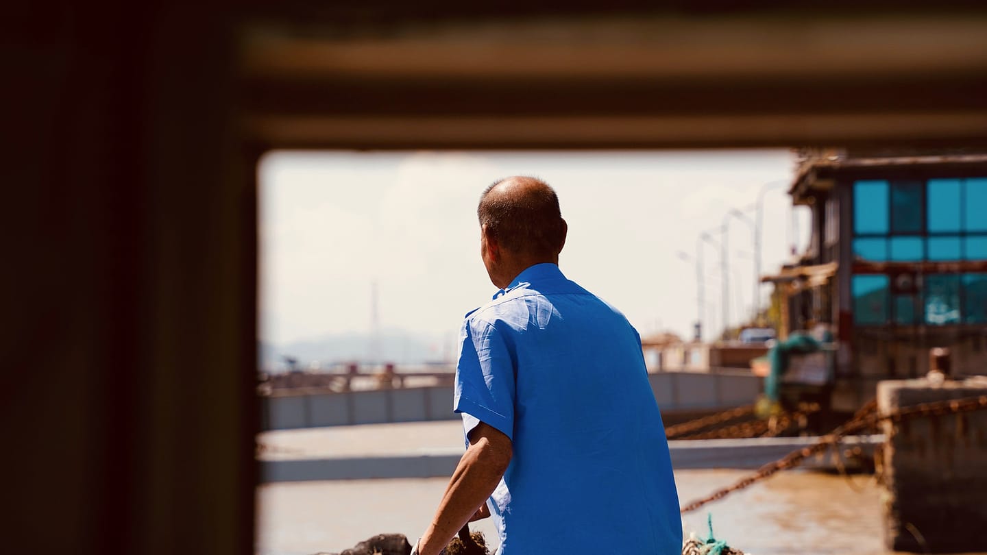 A sailor handles a dock line from a working position near the waterfront.