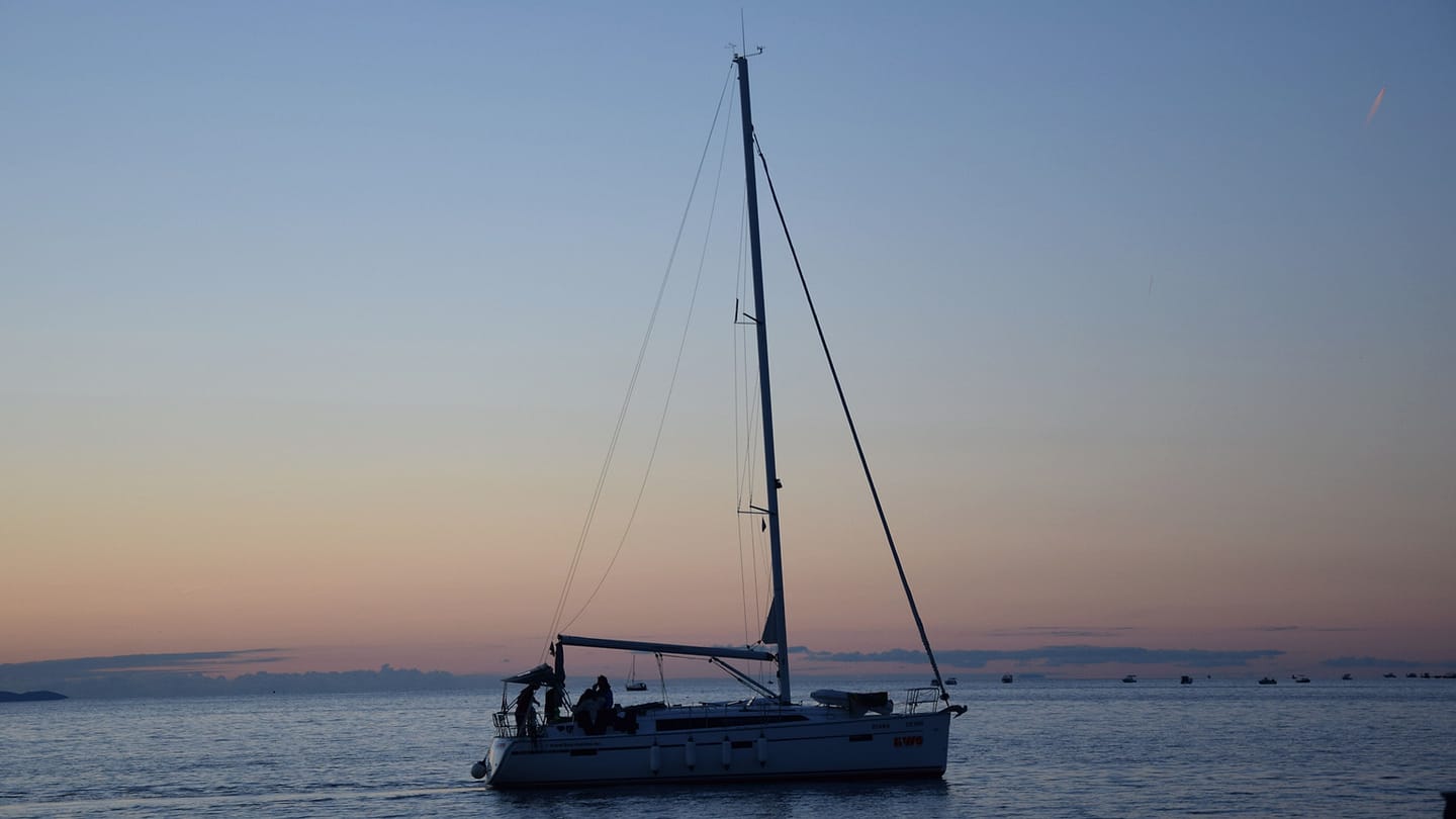 A cruising sailboat on calm water at dusk