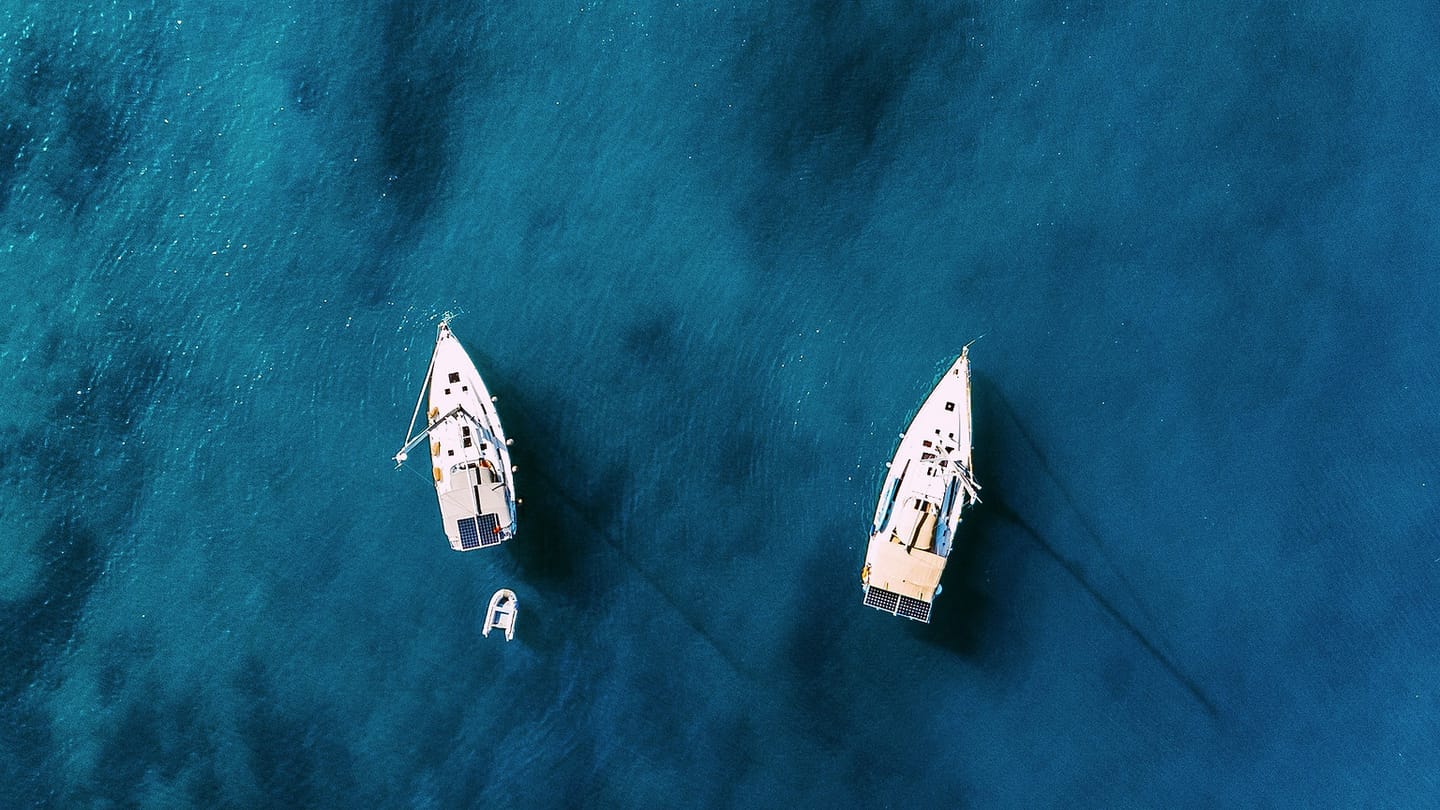 Two sailing yachts anchored in clear coastal water