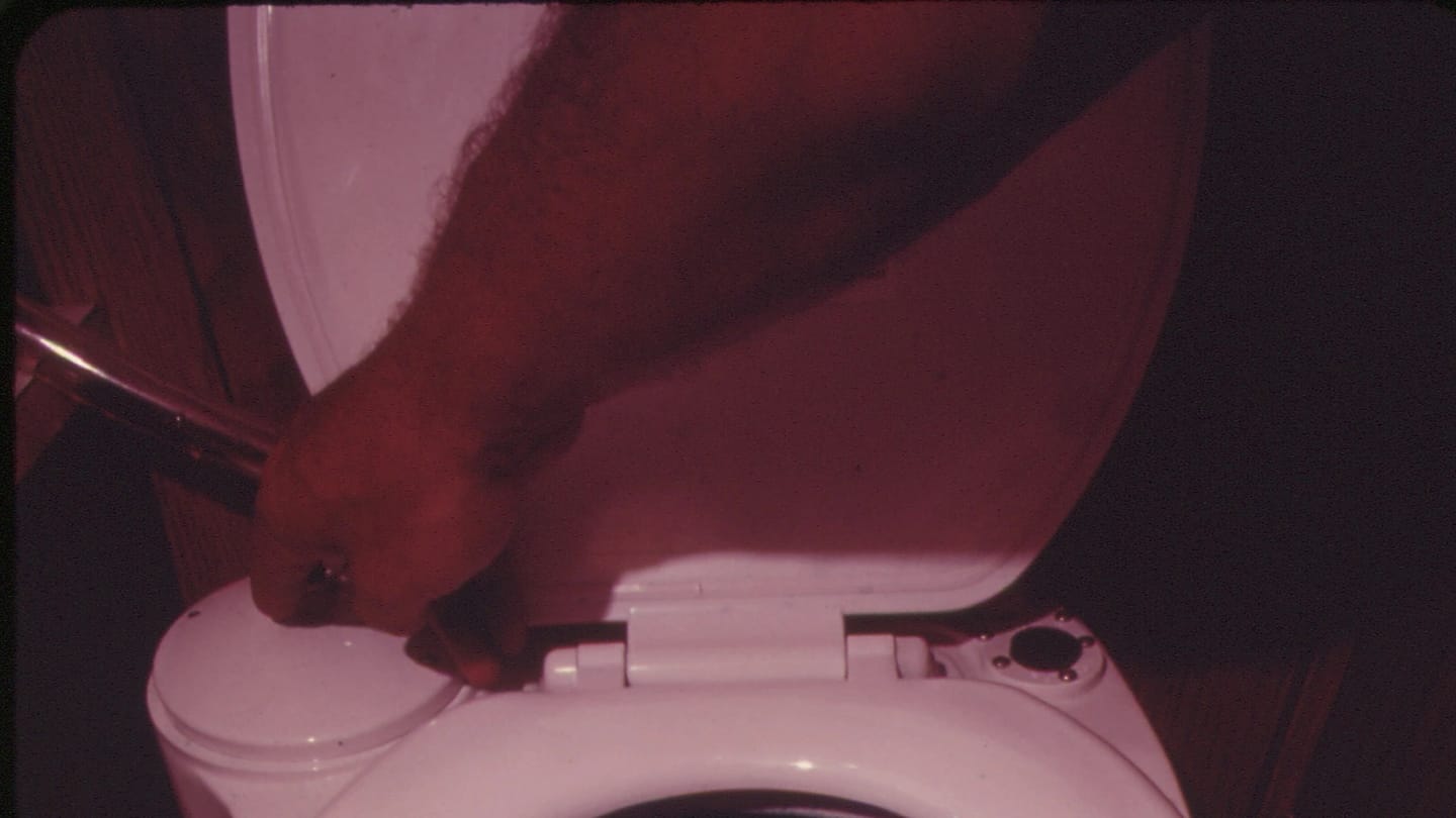 A hand operating the flush control on a marine toilet
