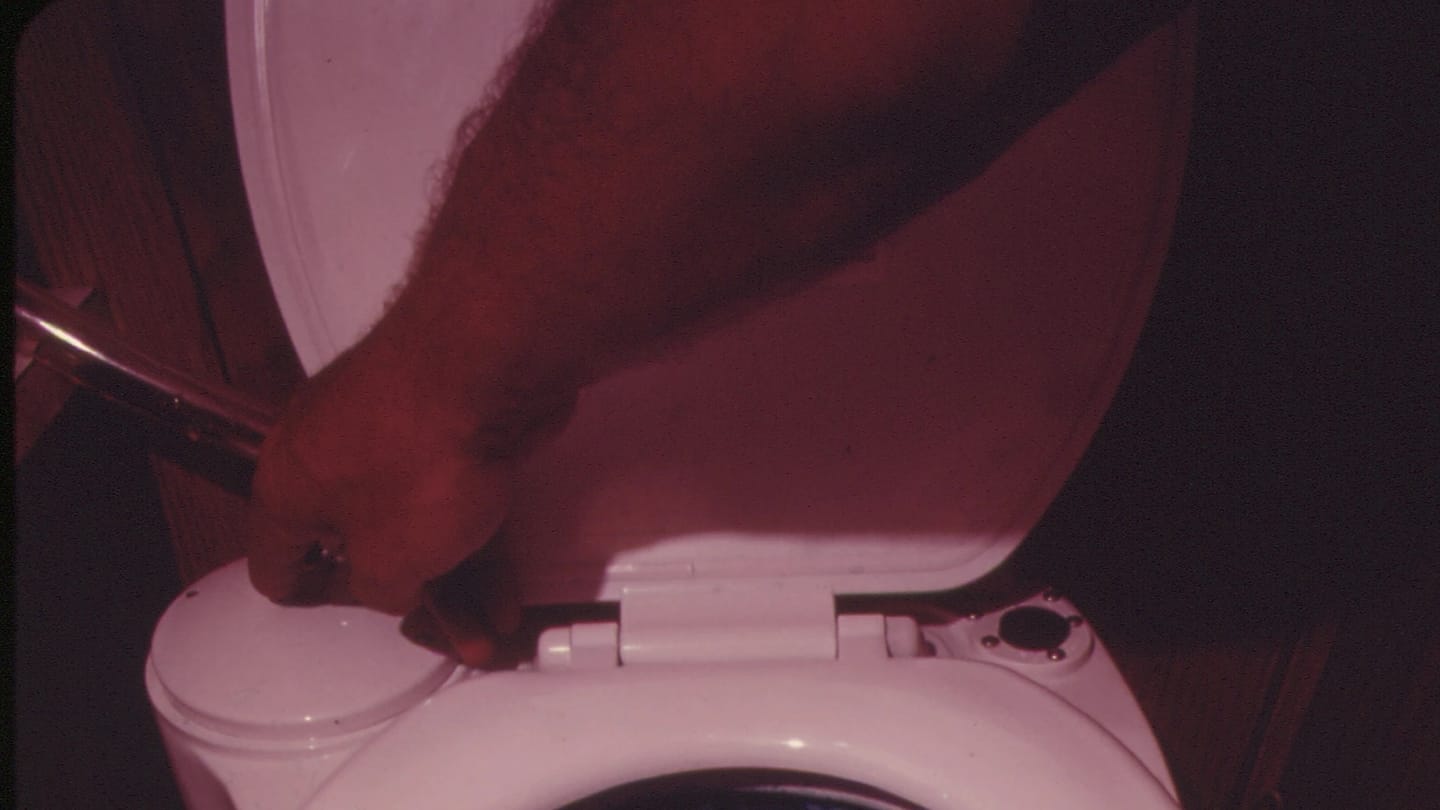 A hand operating the flush control beside a marine toilet bowl