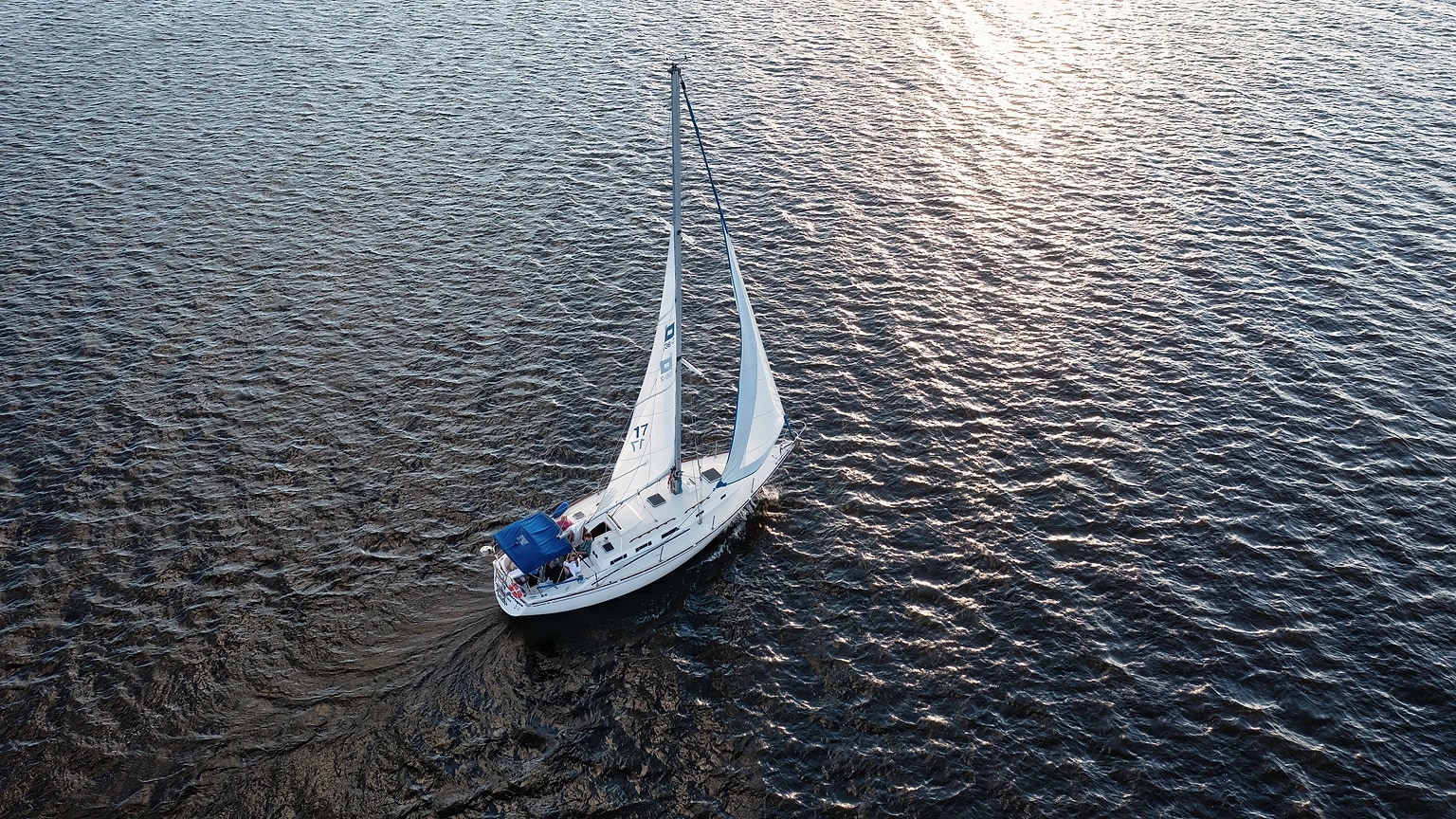 Cruising sailboat crossing open water beneath broken clouds