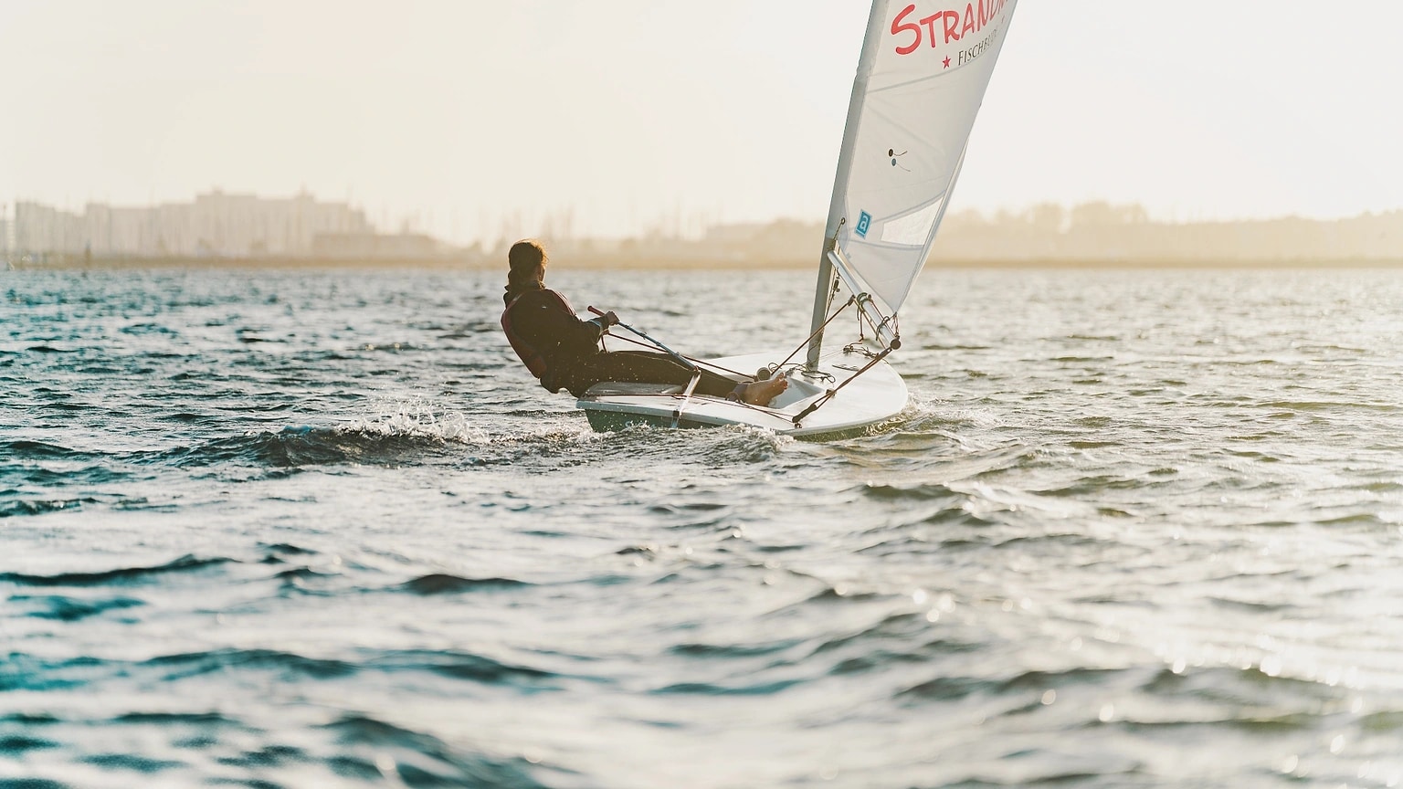 Single sailboat moving across open water near a shoreline