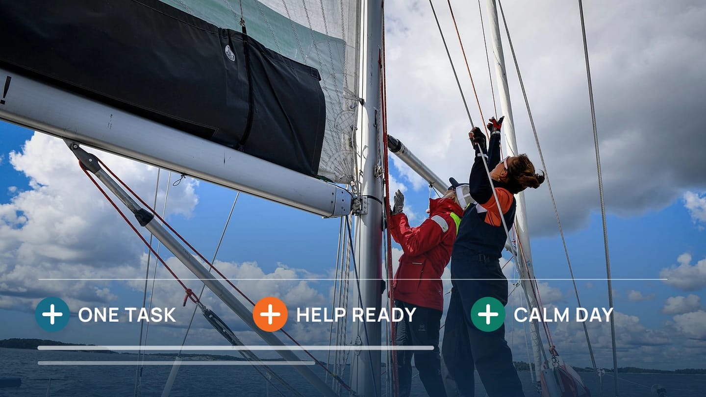 Two sailors work together at the mast of a sailing boat