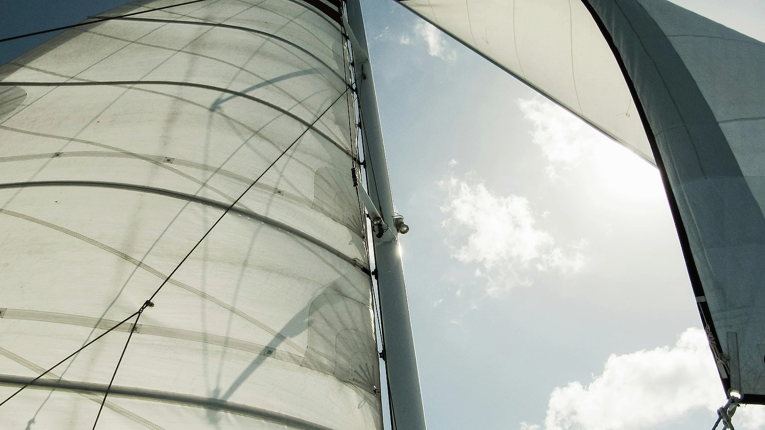 Sunlight shines through filled sails viewed from the deck of a boat sailing upwind