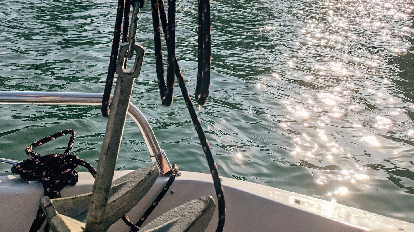 A person holds an anchor and line above the water from a boat.