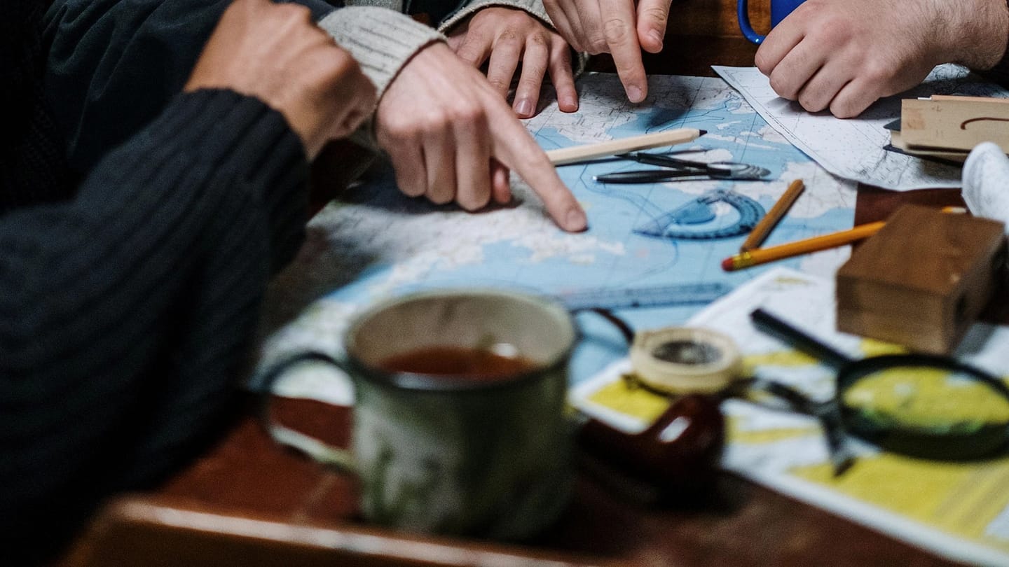 Three people study a paper map together aboard a boat.