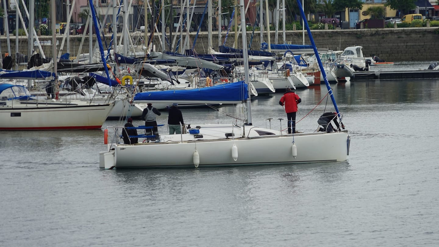 Several people aboard a sailboat in a crowded marina