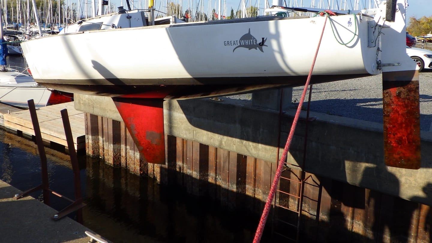 A white sailboat sits ashore with its red fin keel fully exposed below the hull.