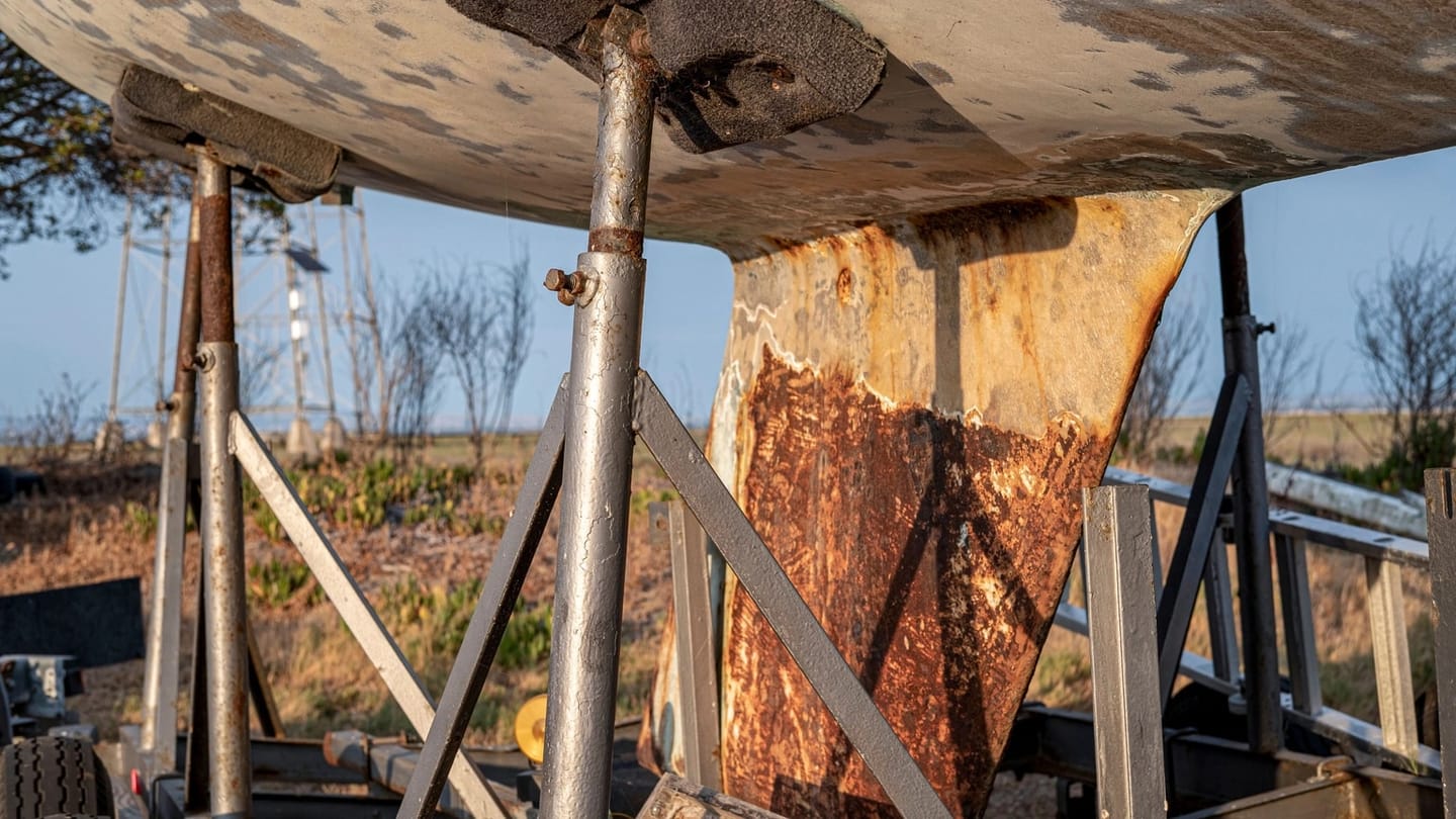 A rust-streaked fin keel stands below a hauled hull, with the entire keel-to-hull junction visible above it.
