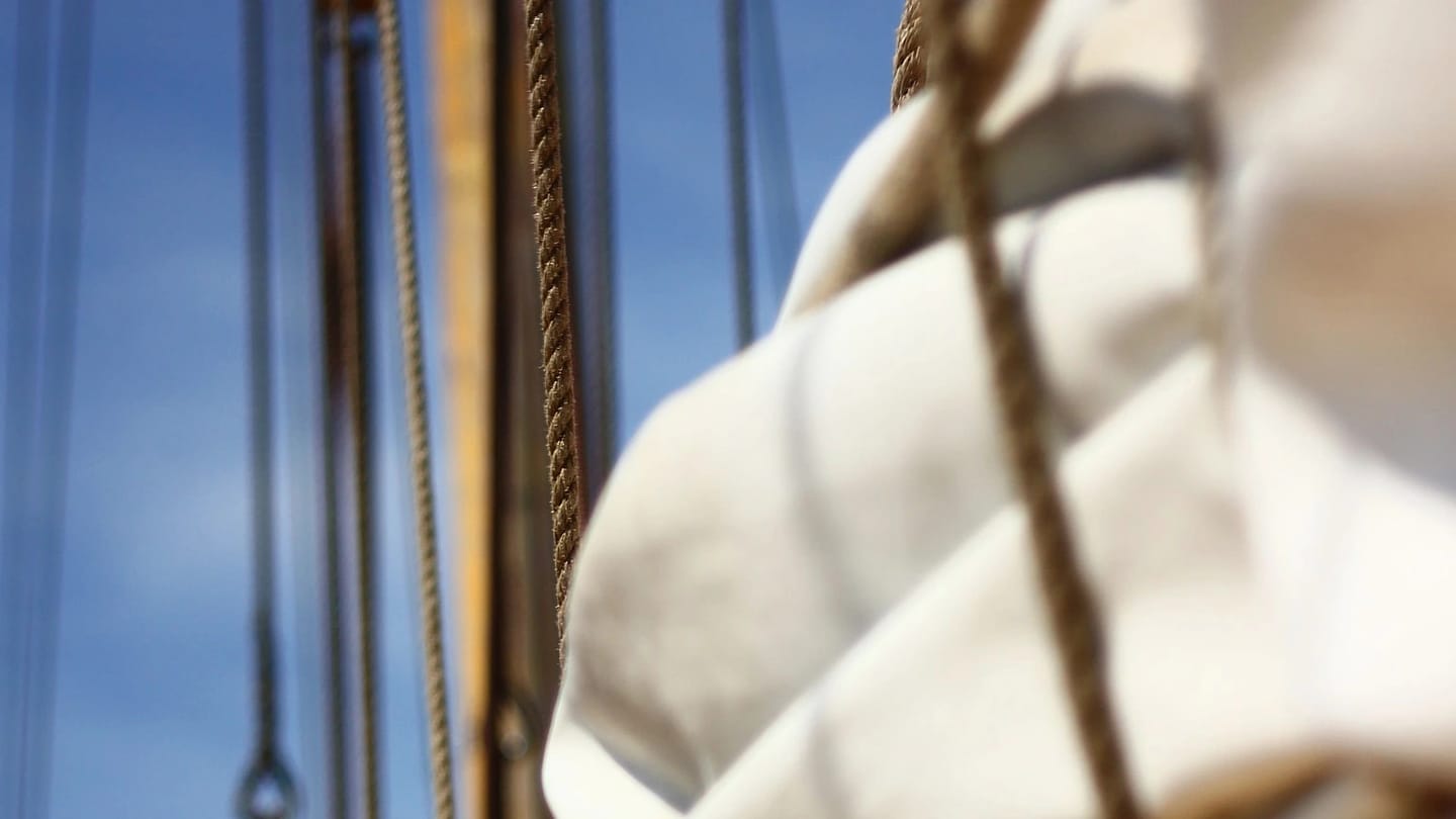 Close sailcloth and rope run vertically against a blue sky.