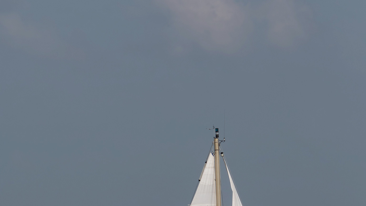 Sailing crew members work together near the mainsail and cockpit.