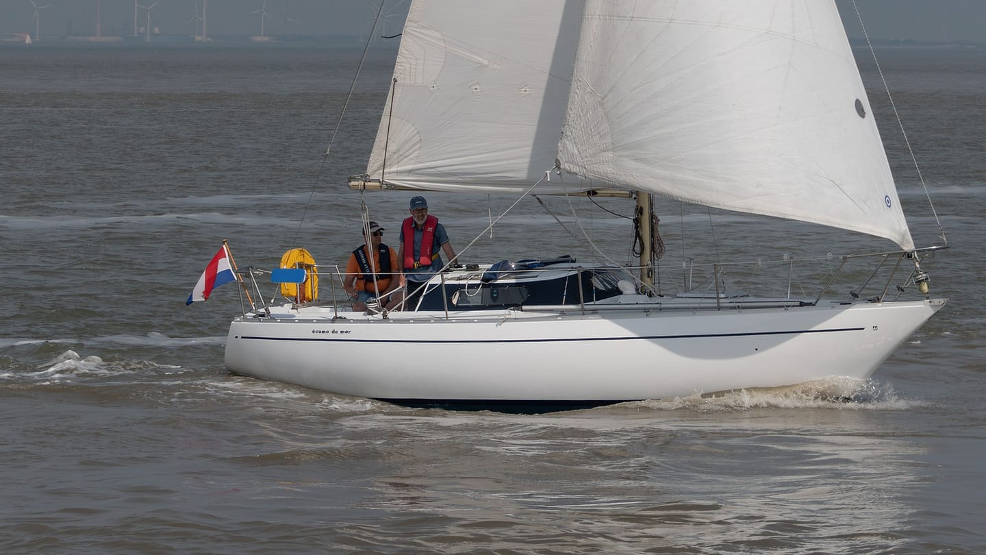 A small sailboat moves across open water with a sailor aboard.