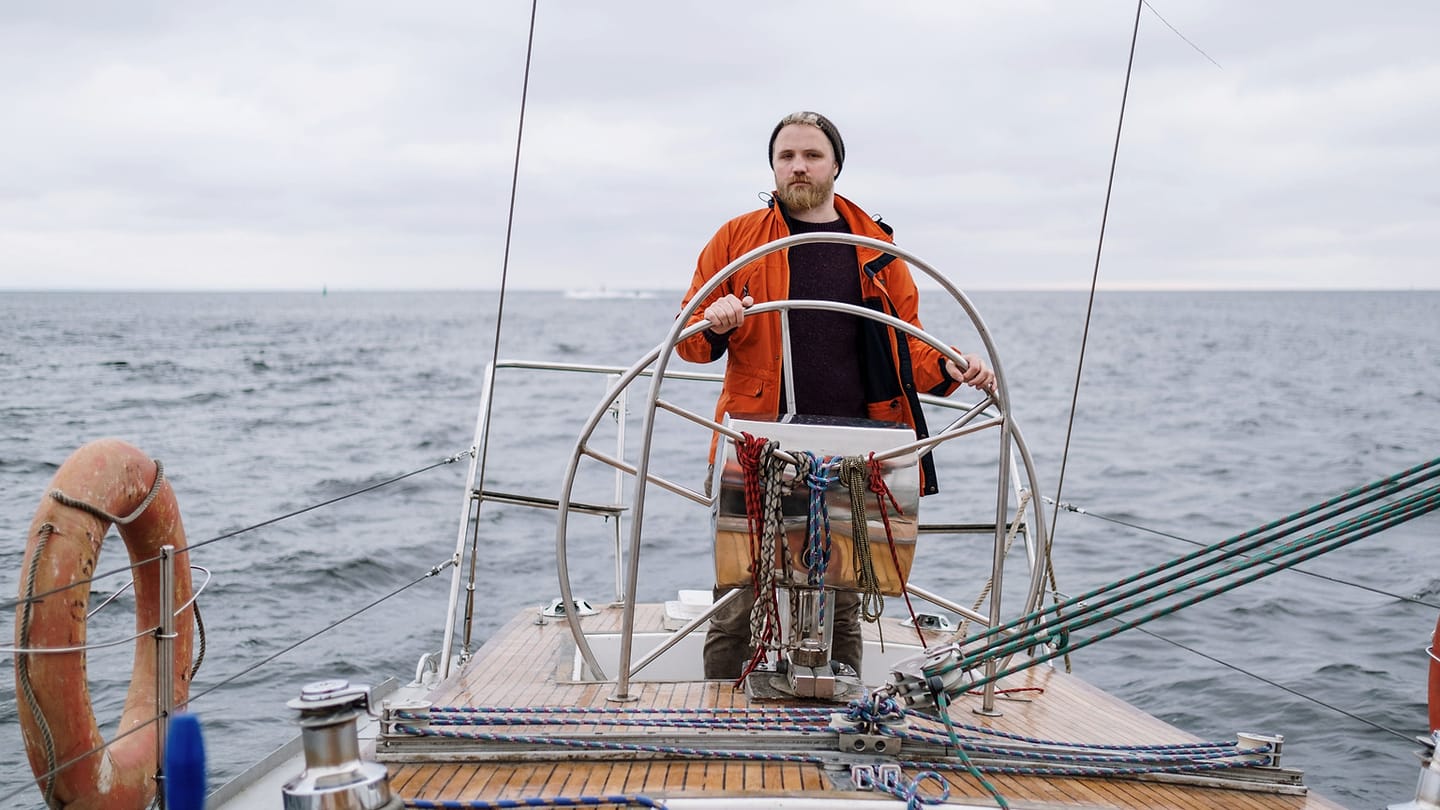 A close view of a sailor managing a line on a sailboat deck.