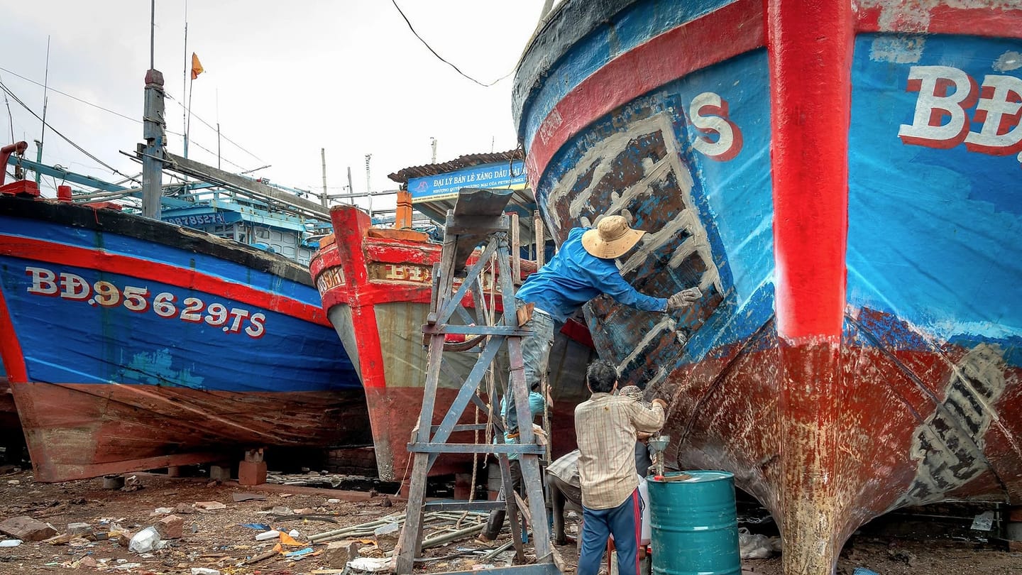Workers repairing the side of a boat in a yard