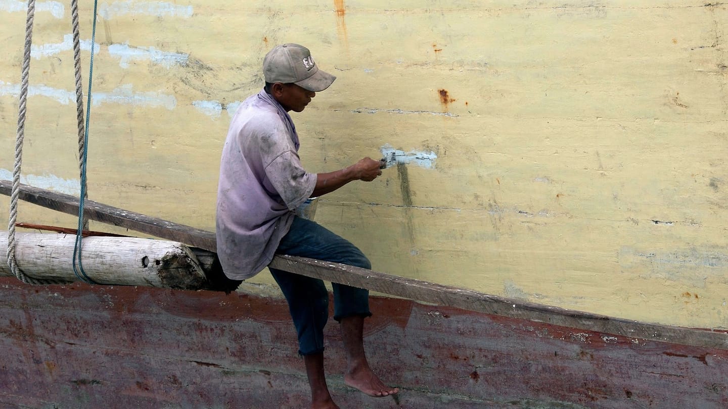 Person painting the side of a boat outdoors
