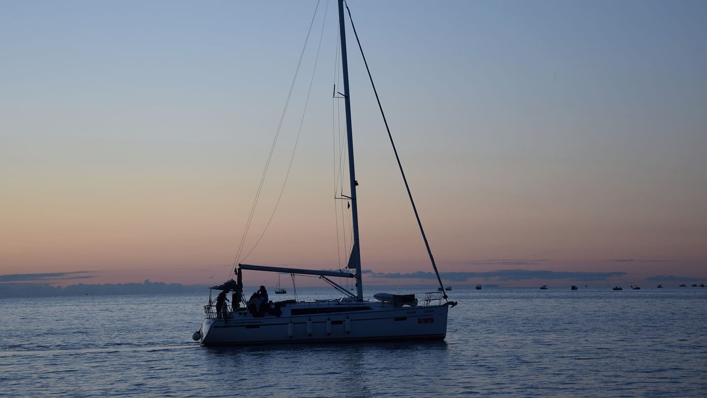 A cruising sailboat moves slowly across calm evening water.