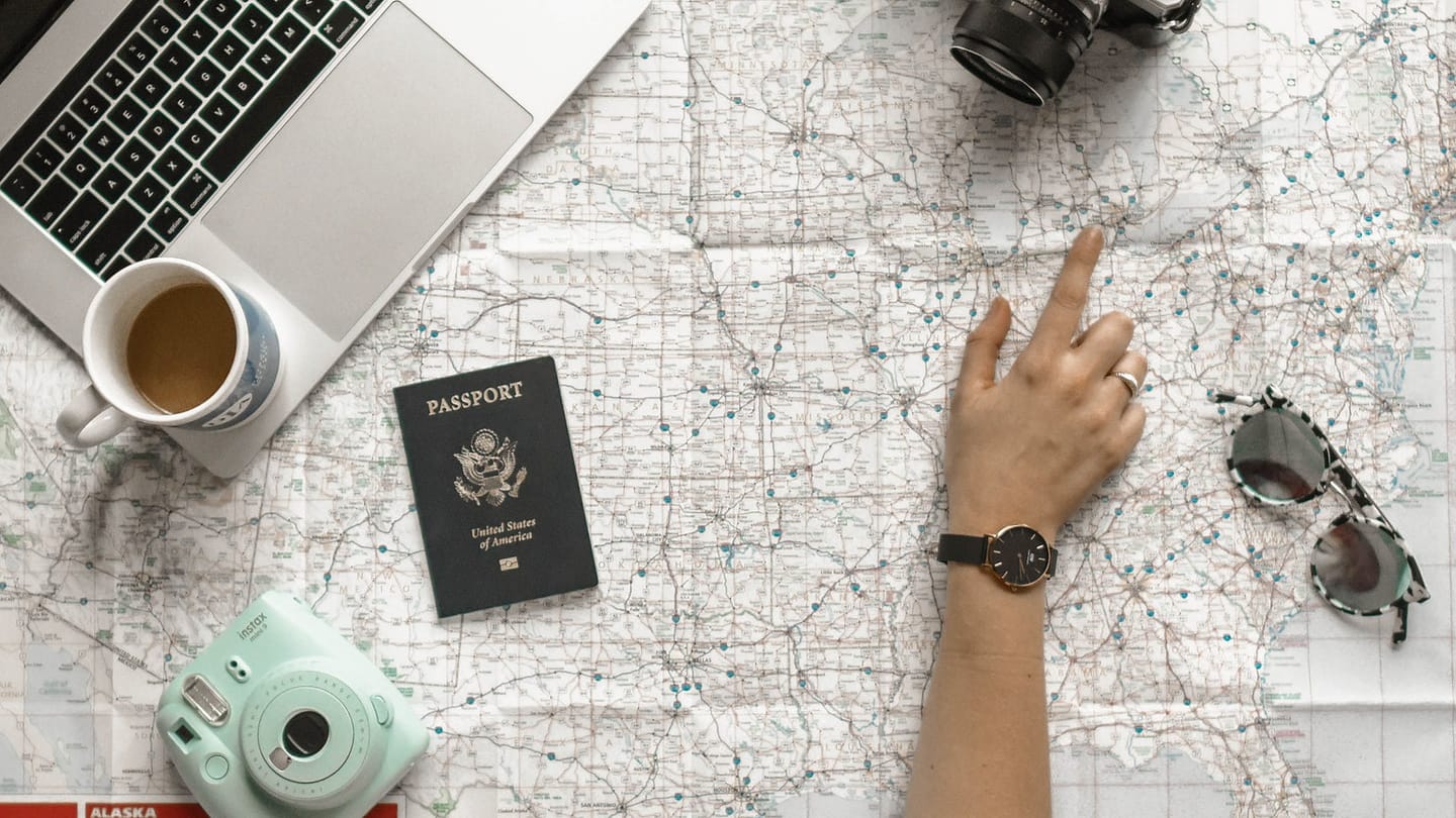 A map, laptop, passport, and camera laid out for trip planning
