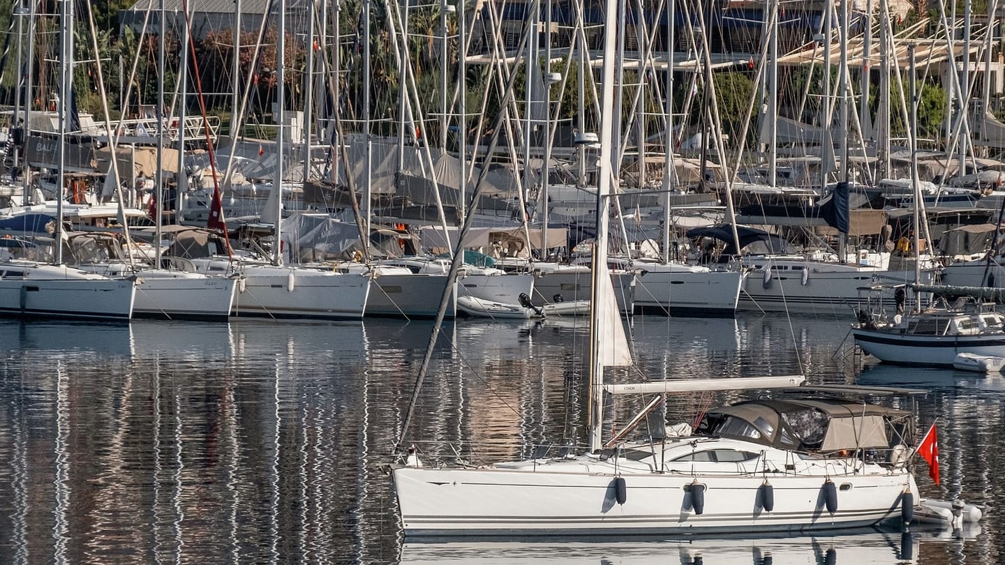 A sailboat moves down a marina fairway among moored boats.