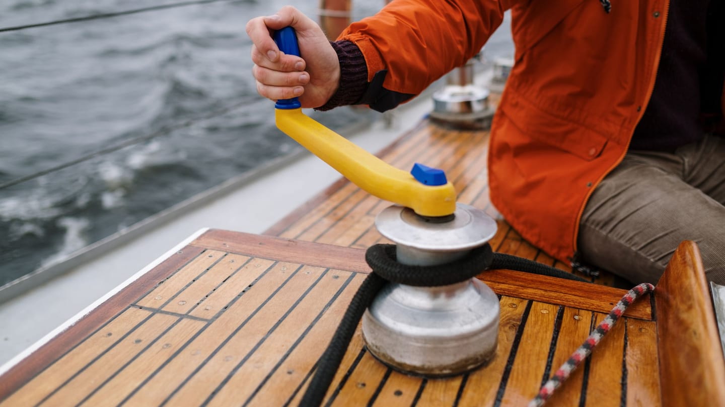 A sailor turns a winch handle beside a loaded line on deck