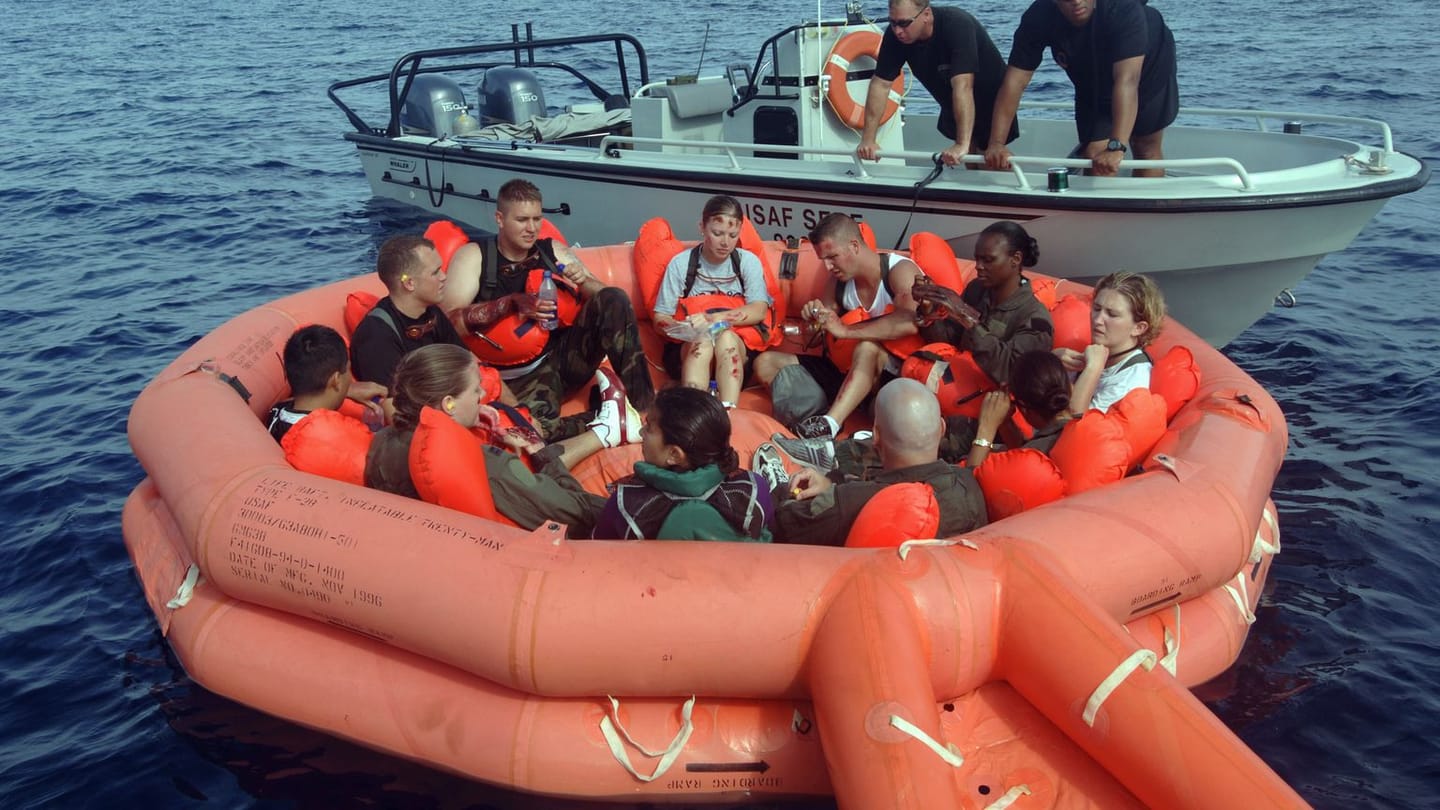 People wearing lifejackets seated in an inflated life raft beside a rescue boat