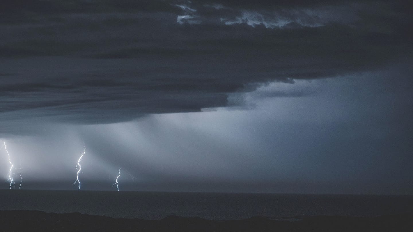 Several lightning bolts descend from a dark thunderstorm over the sea.