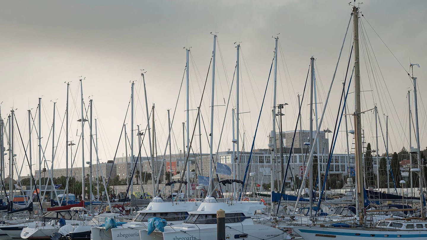 A tall sailboat mast and rigging stand above a marina, showing the conductive structure a system must address.