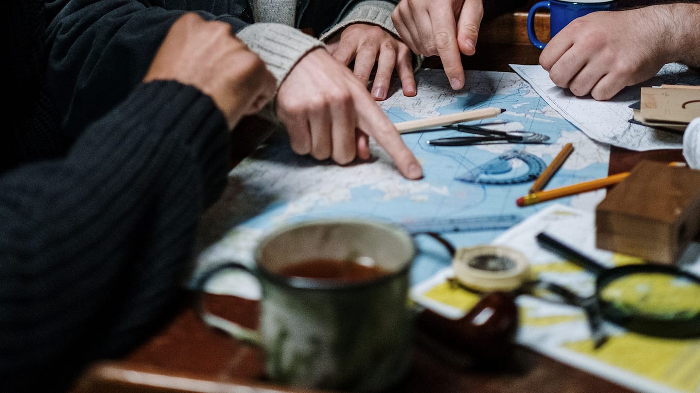 Sailors studying a paper chart at a navigation table