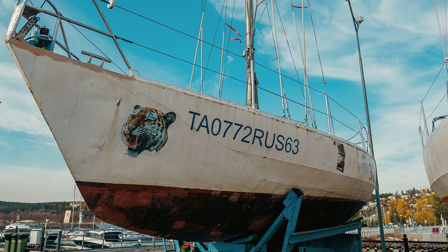 A white sailboat rests on supports in a boatyard with its keel visible.