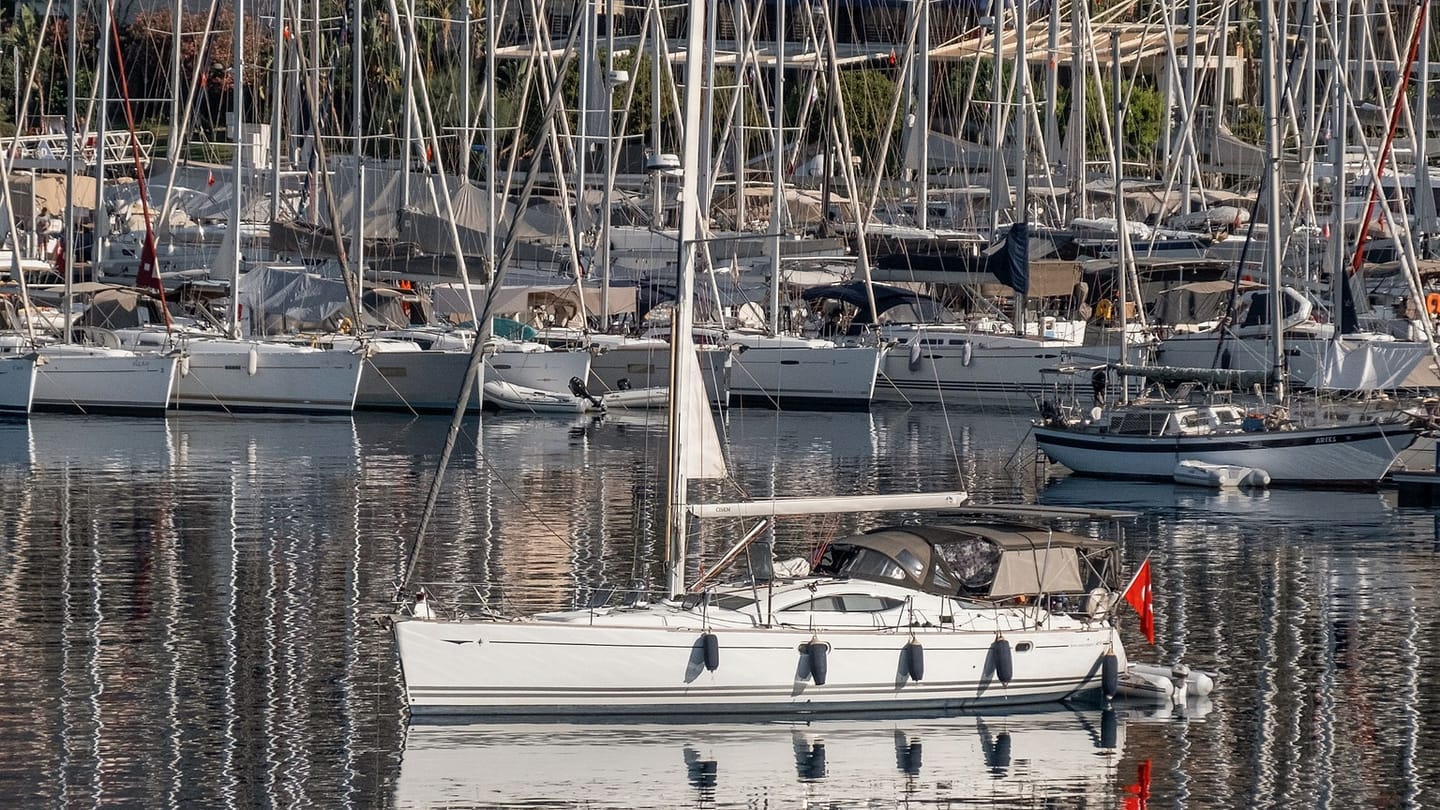 A white sailboat motors between rows of moored boats in a marina.