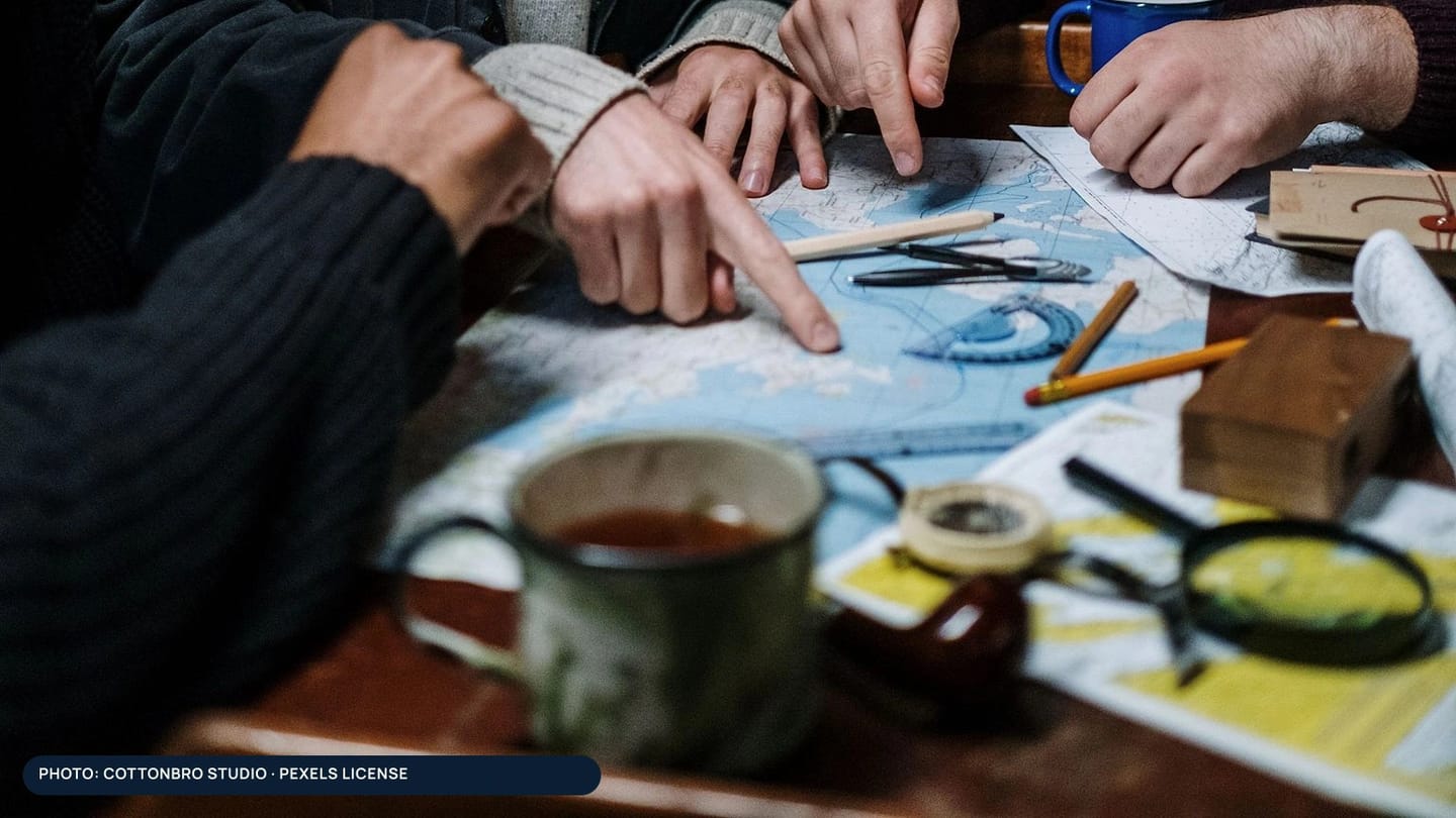 Hands comparing route notes over paper charts before a sailing trip