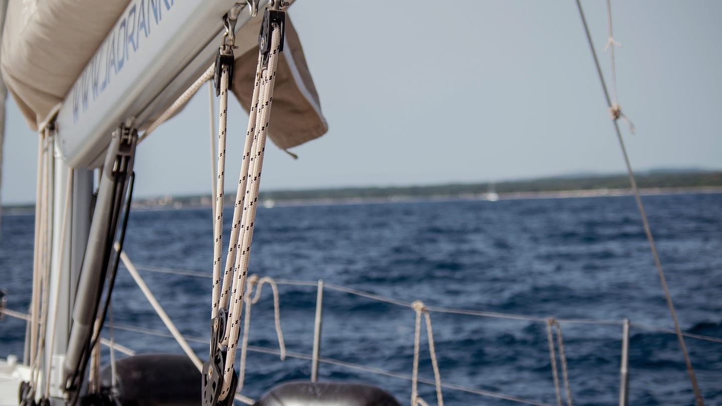 Several ropes run beside metal fittings on a white sailboat deck.