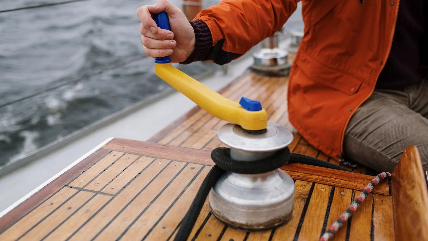 A sailor turns a winch handle beside a loaded working line.