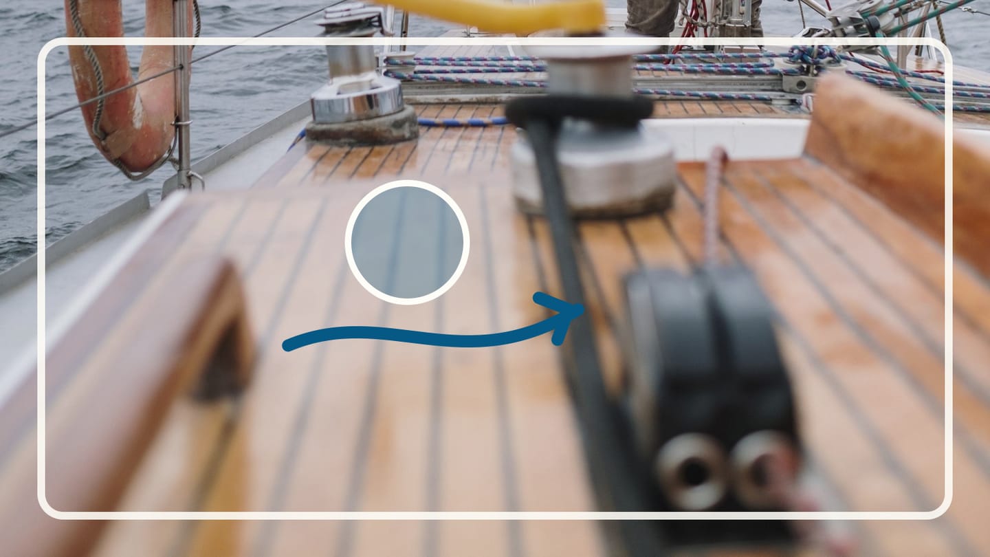 Shallow-focus view of a wooden sailboat deck with a winch and black deck fitting