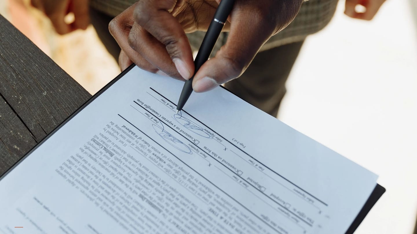 Hand signing a charter-style agreement beside stacked documents