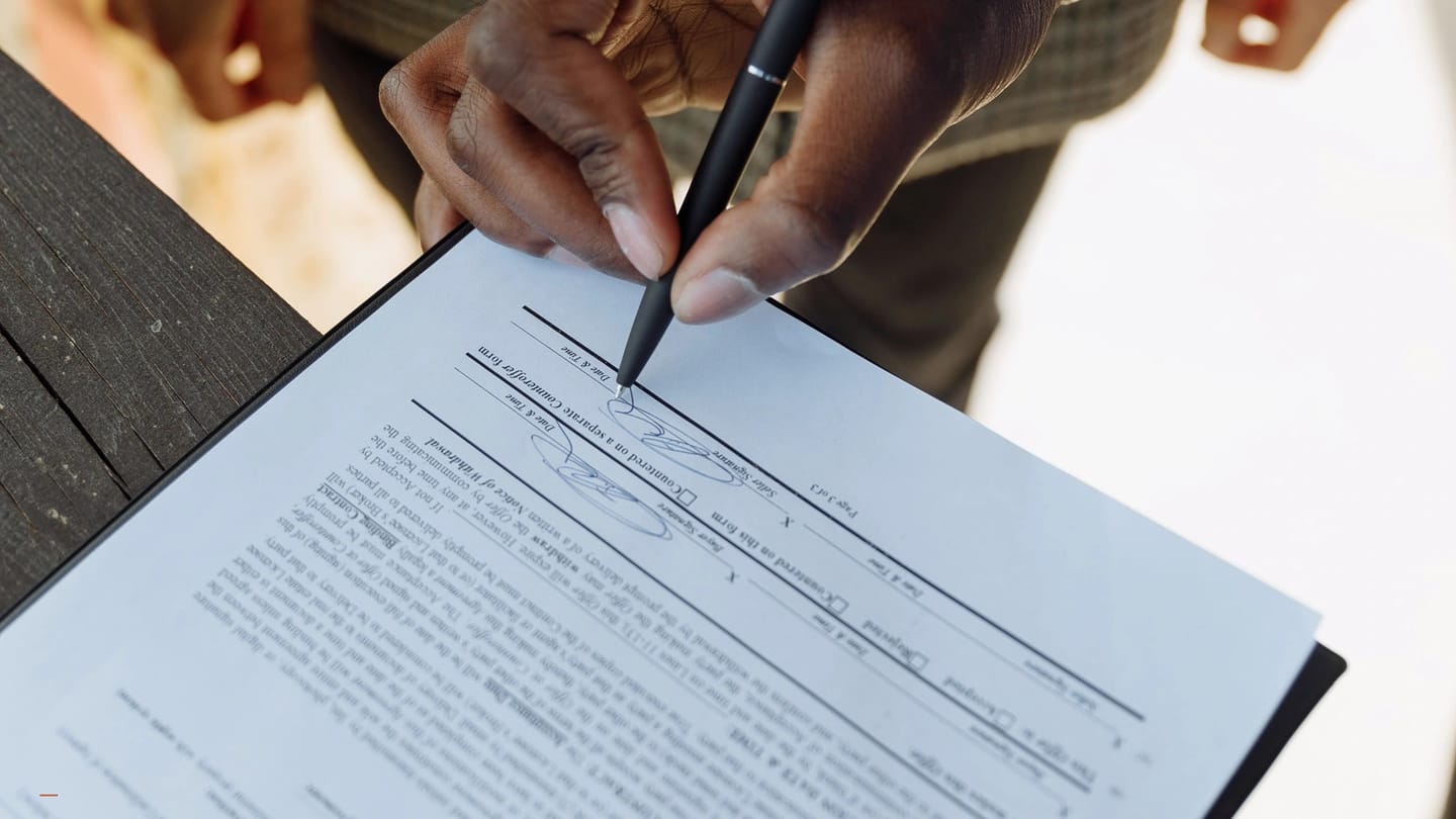 Person signing a printed agreement at a wooden desk